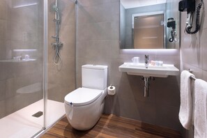 A modern bathroom with a glass-enclosed shower, a white toilet, a sink with a mirror above it, and a towel hanging on the wall.