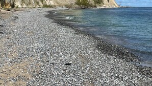 A pebbled beach with cliffs and a clear sky.
