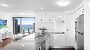 A modern kitchen with white cabinets, stainless steel appliances, and a large island. - Chevron Renaissance Ocean & River Views (Surfers Paradise)