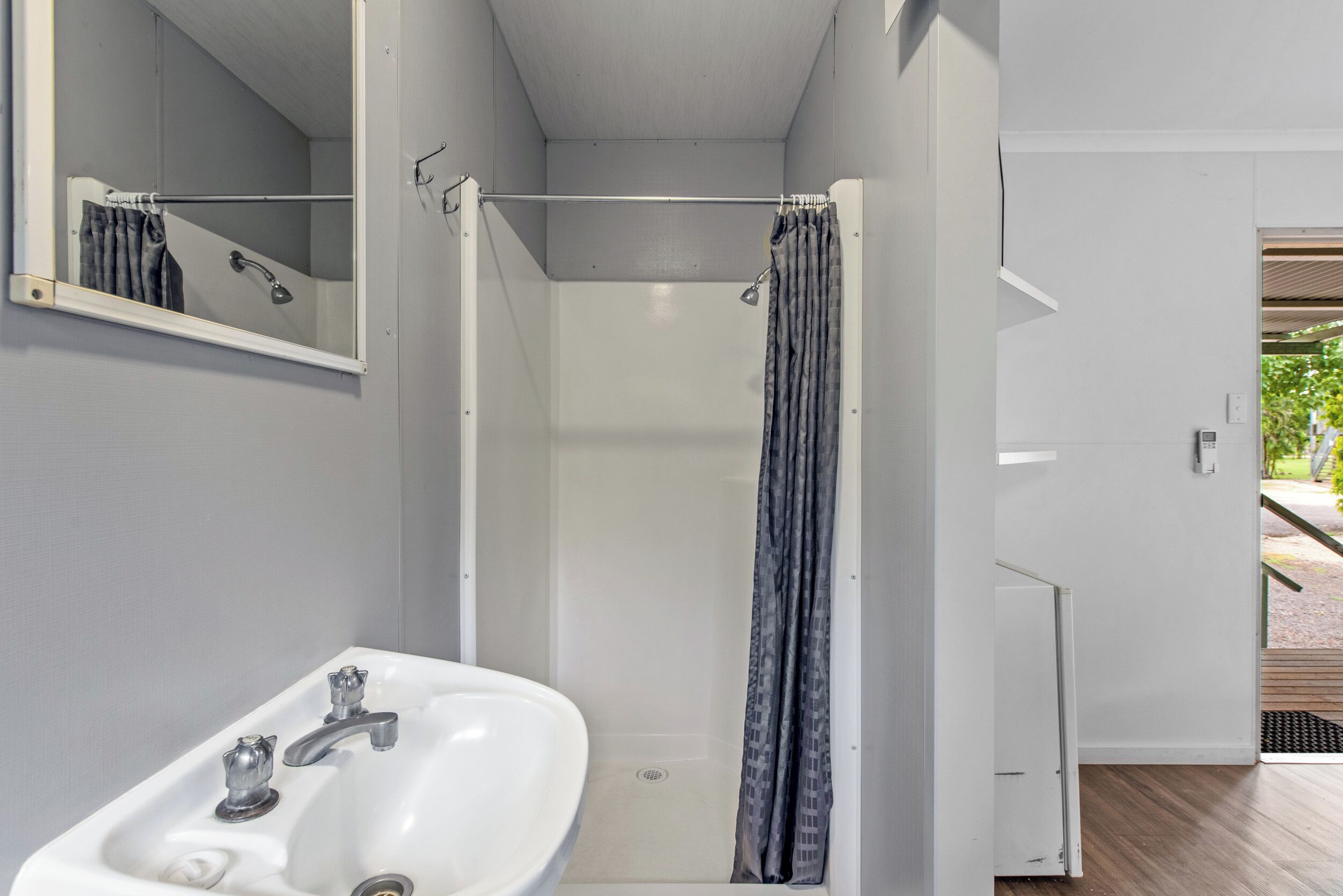 A bathroom with a white sink, a mirror, a shower with a curtain, and a door leading to another room.