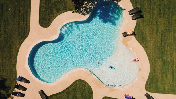Vista aérea de una piscina de forma singular, rodeada de arena y equipada con varias sillas de descanso.