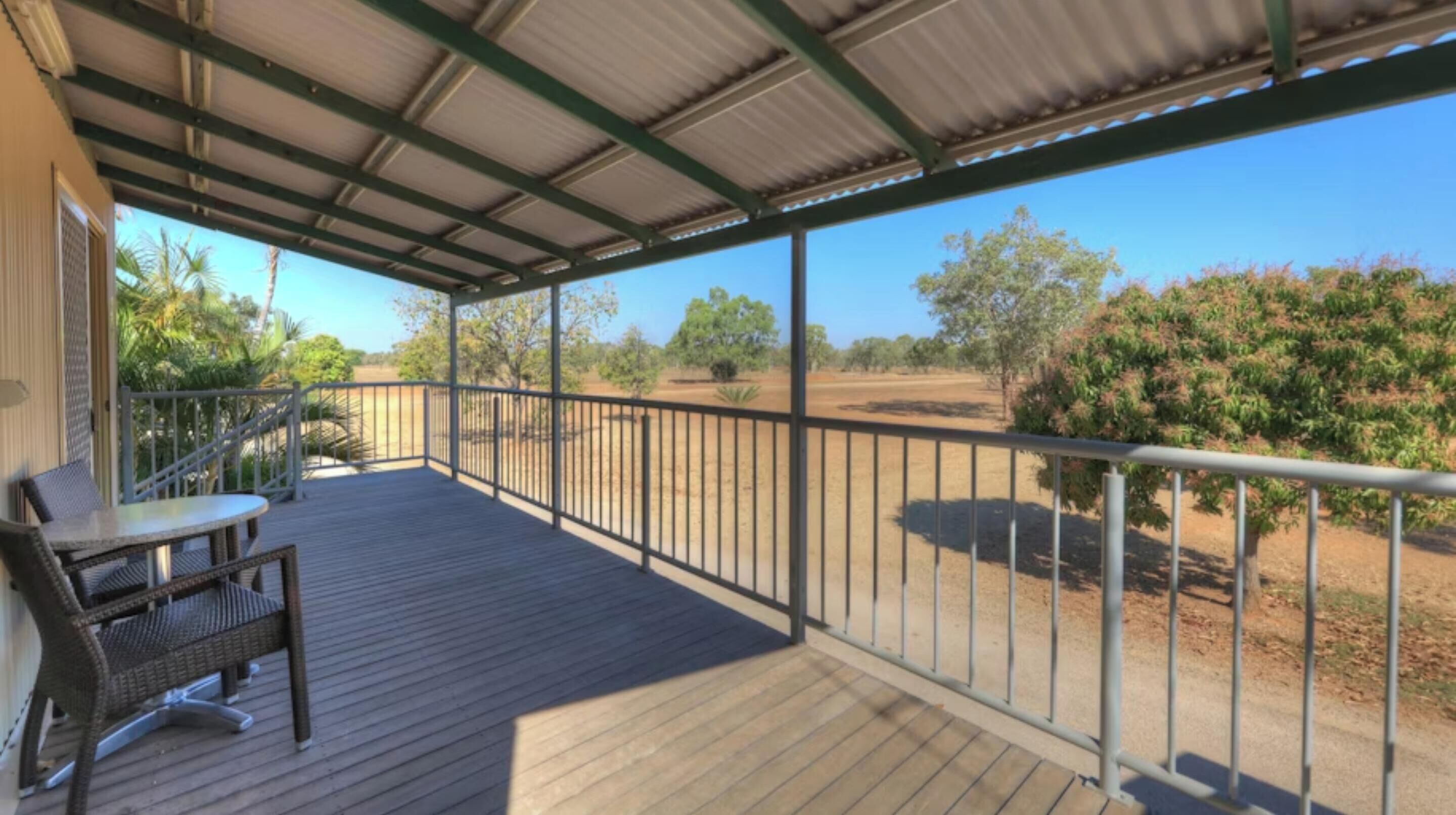 A covered outdoor area with a wooden deck, metal railing, and a table with chairs.