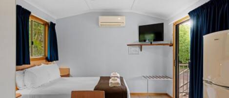 A compact hotel room with a bed, a small table, a TV mounted on the wall, and a refrigerator.