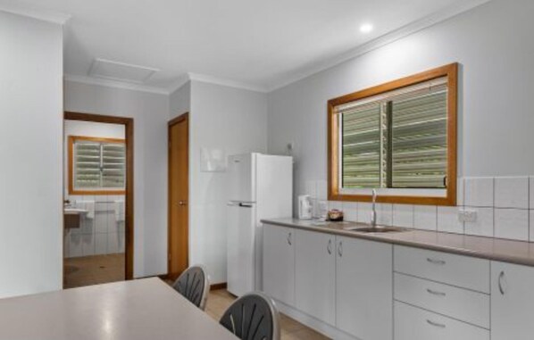A modern kitchen with white cabinets, a built-in refrigerator, a window with blinds, and a dining area with a table and chairs.
