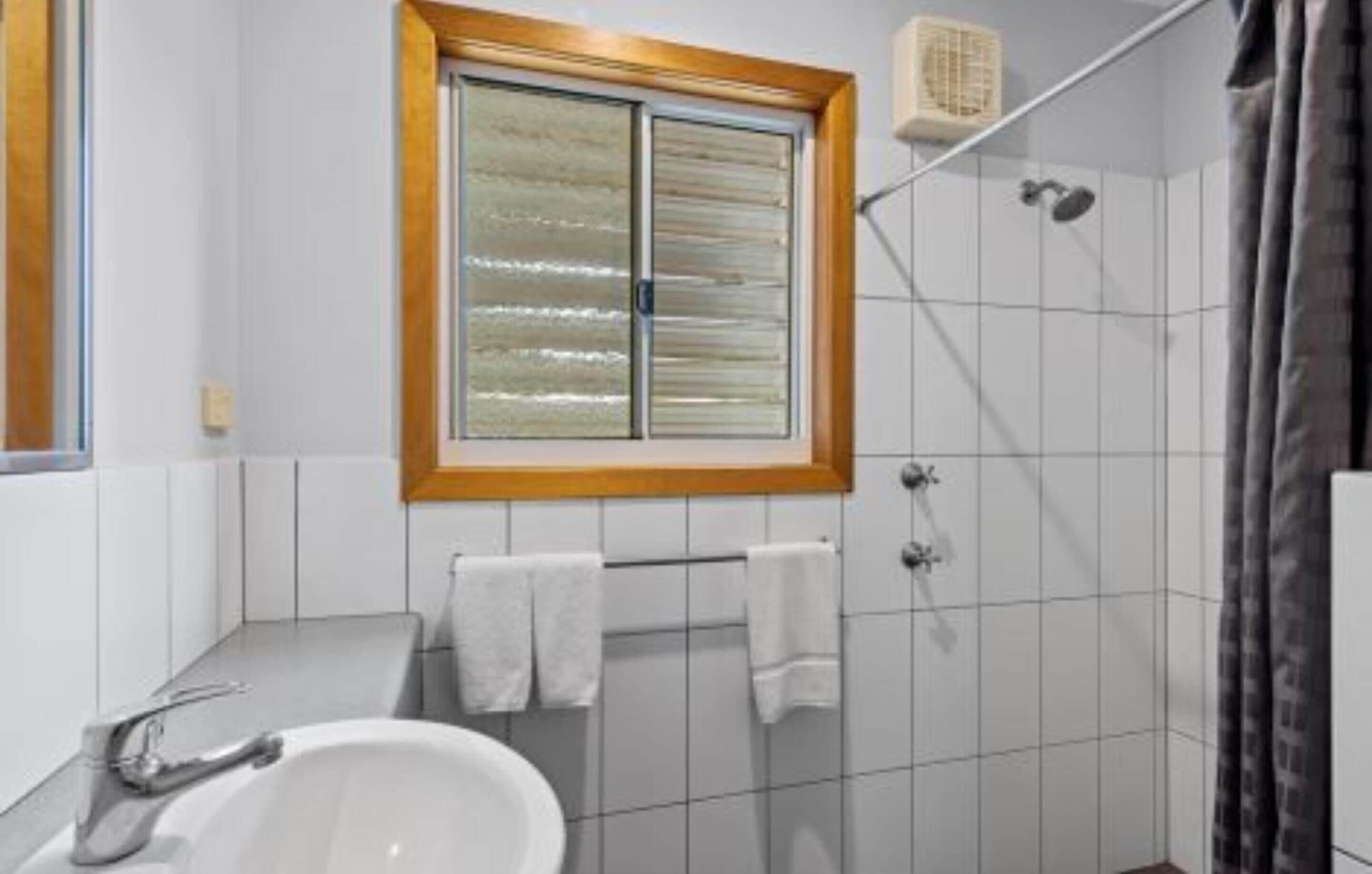 A bathroom with a window, a shower, and a sink.