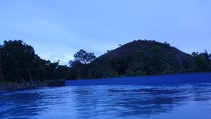 Ruhige Wasserfläche mit einer blauen Barriere und einer mit Bäumen bewachsenen Hügelkette im Hintergrund.