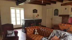 A living room with a brown leather sofa, a red armchair, a plaid blanket, and a glass of water on a wooden table.