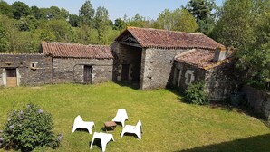 A stone building with a tiled roof, surrounded by a grassy area with white plastic chairs.