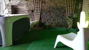 A room with a stone wall, a green artificial turf floor, a white chair, and a wooden ladder.