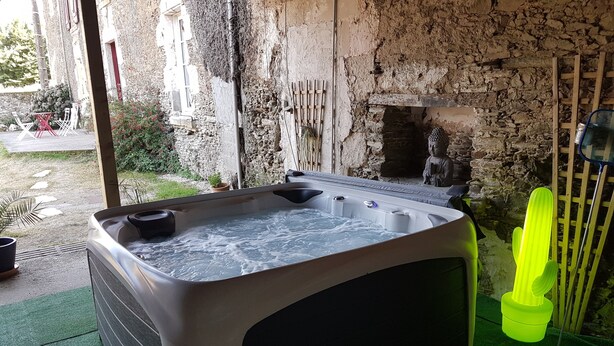 A hot tub in a rustic outdoor setting with stone walls and a small Buddha statue.
