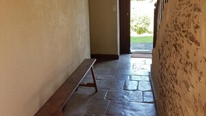 A narrow hallway with a wooden bench, a metal hookboard, and a stone floor.