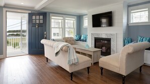 A living room with a fireplace, a television mounted above it, and a door leading to a balcony. - Luxury Monument Beach Villa /Short term rentals (Bourne)