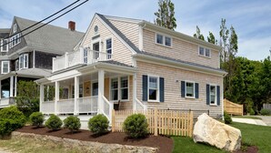 A two-story house with a covered porch, a stone retaining wall, and a large rock in the front yard. - Luxury Monument Beach Villa /Short term rentals (Bourne)