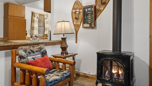 Ein gemütliches Wohnzimmer mit einem Holzstuhl, einem kleinen Tisch mit Lampe, einer Wanddekoration mit Fischen und einem schwarzen Kaminofen.