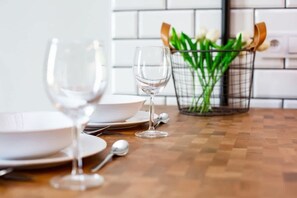 A dining table set with white plates, bowls, and wine glasses, accompanied by a metal basket containing green plants.