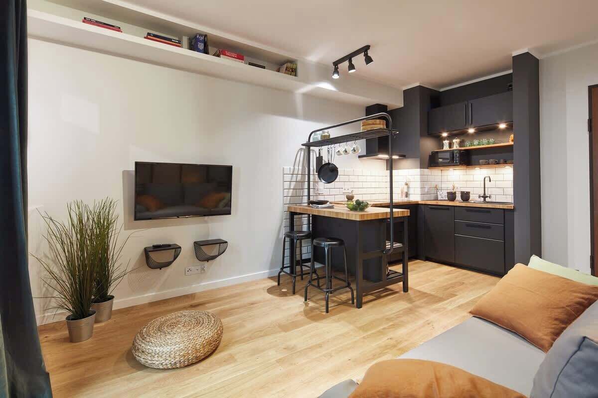 Un espacio habitable compacto con kitchenette, un televisor montado en la pared y una zona de estar acogedora con cojines.