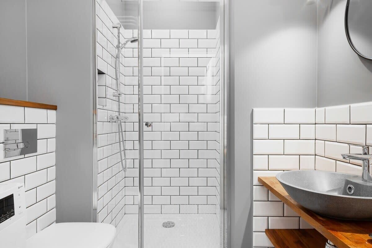 A modern bathroom with white subway tiles, a glass-enclosed shower, a white toilet, and a wooden vanity with a sink.