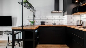 A modern kitchen with black cabinets, a wooden countertop, and a black hanging rack with cups. - Modern Apartment with Balcony | Close to the Metro (Warszawa)