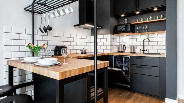 A modern kitchen with black cabinets, a wooden countertop, and a built-in dishwasher. - Modern Apartment with Balcony | Close to the Metro (Warszawa)