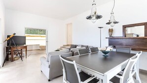 Una sala de estar moderna con comedor, una escalera y un ventanal grande.