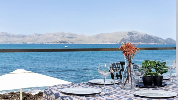Mesa dispuesta para comer con vistas al mar y montañas de fondo.