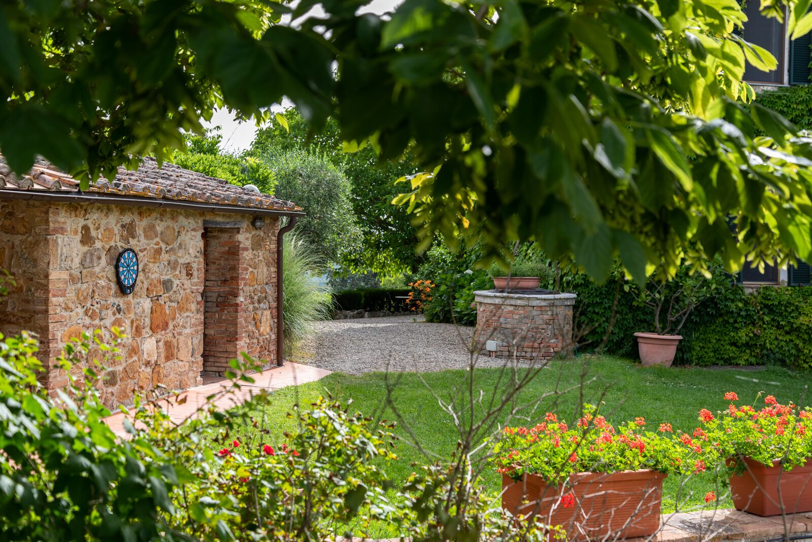 Un bâtiment en pierre doté d’un jeu de fléchettes, entouré d’un jardin bien entretenu avec des plantes en pot et un chemin de gravier.