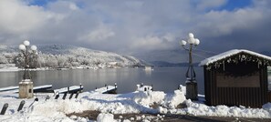 A snow-covered dock with boats, a small shed, and a hill in the background. - Apartment with a view of Lake Wörthersee - Gallery (Velden am Wörthersee)
