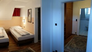 Una habitación con dos camas individuales, un ventanal con cortina roja, una lámpara de pared y un armario de madera.