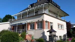 Una casa de dos pisos con un balcón, una chimenea y un jardín con plantas en macetas.