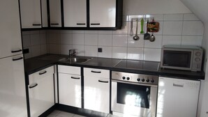 Una cocina con armarios blancos, un lavamanos de acero inoxidable, un microondas y un lavavajillas.