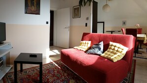 Una sala de estar con un sofá rojo, un televisor sobre un mueble blanco y una mesita.