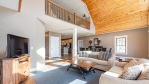 A spacious living area with a wooden ceiling, a flat-screen TV on a wooden cabinet, a sofa, and a coffee table. - Elevated Dog Friendly Escape w/ Hot Tub & Fire Pit (Oakland)