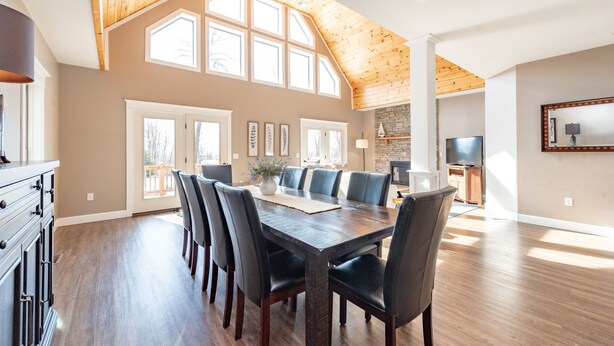 A spacious dining area with a high wooden ceiling, large windows, and a stone fireplace. - Elevated Dog Friendly Escape w/ Hot Tub & Fire Pit (Oakland)