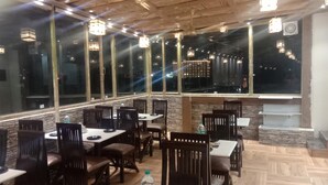 A restaurant with wooden ceiling and large windows offering a city view. Tables are arranged with chairs. - Shivaay Grand (Amritsar)