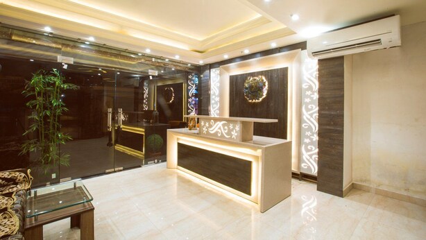 A reception area with a modern design, featuring a reception desk, a glass partition, and a decorative wall with a circular emblem. - Shivaay Grand (Amritsar)