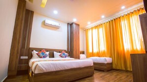 A hotel room with two wooden beds, a large window with yellow curtains, an air conditioning unit, and a wooden floor. - Shivaay Grand (Amritsar)