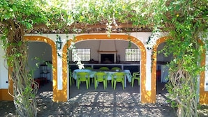 Un'area pranzo all'aperto con tavolo e sedie sotto un arco coperto, immersa nel verde.