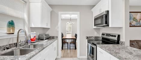 A modern kitchen with white cabinetry, granite countertops, a built-in microwave, and a dishwasher.