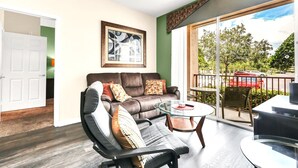 A modern living room with a leather sofa, a glass coffee table, and a view of the outdoors through a sliding glass door.