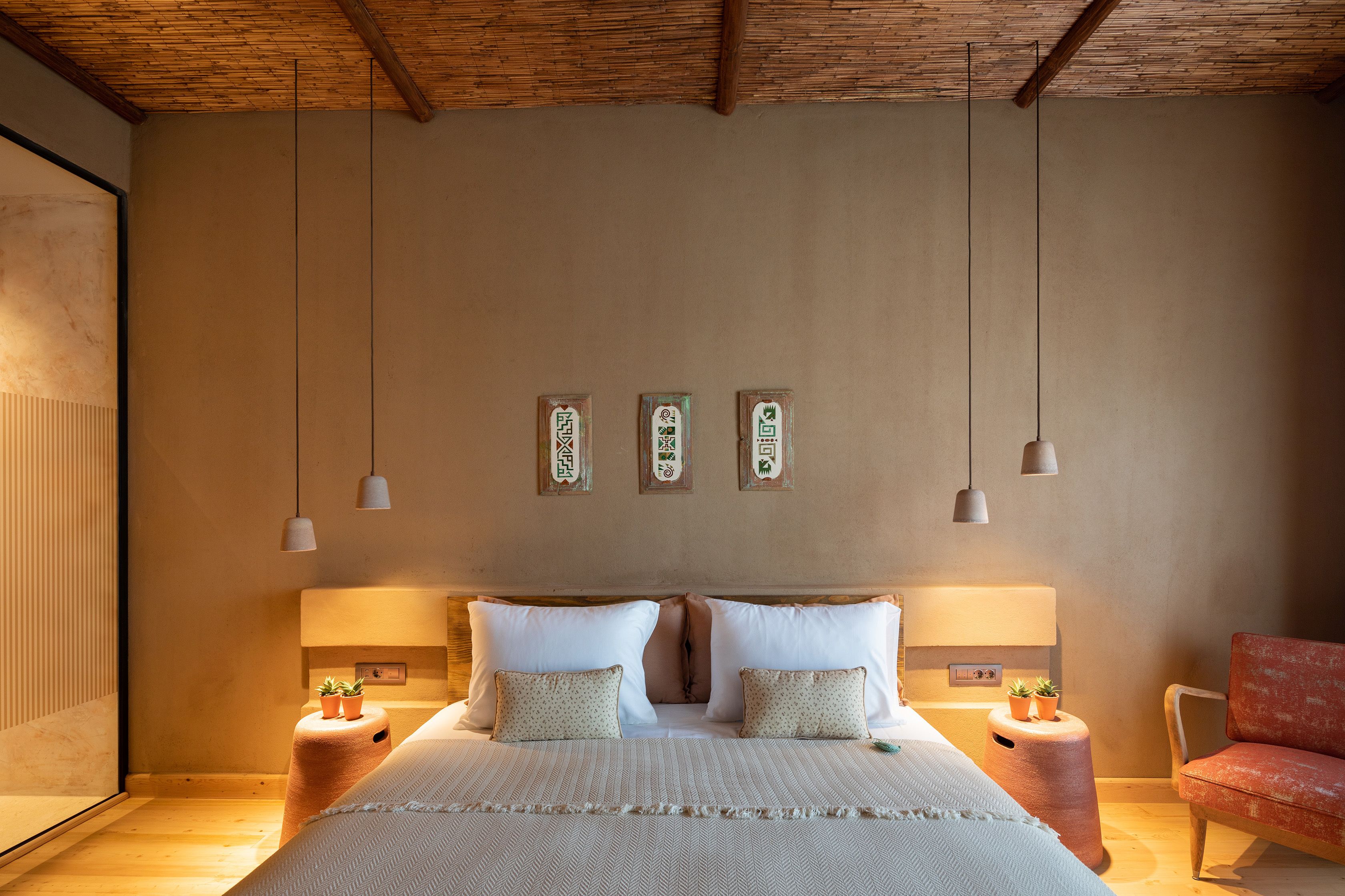 A bedroom with a wooden ceiling, two bedside tables with lamps, a bed with pillows, and a chair.