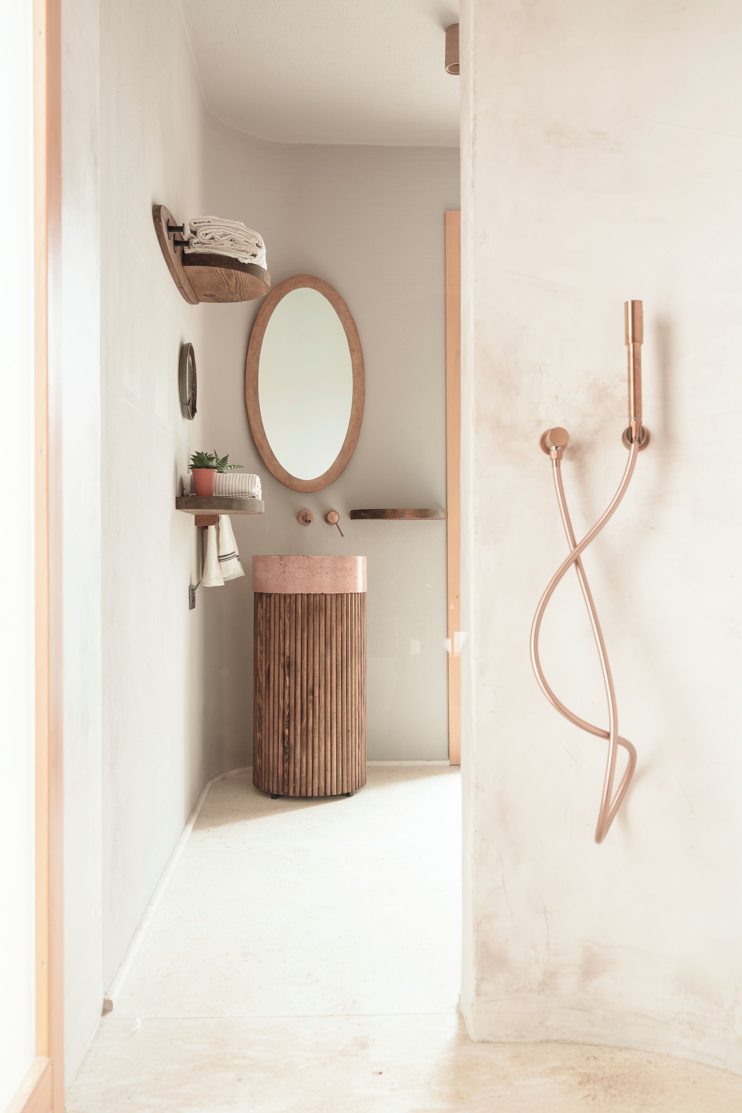 A modern bathroom with a wooden vanity, a round mirror, a towel rack, and a shower with a curved hose.
