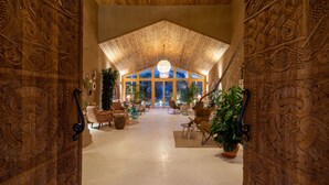 A spacious lobby with intricate wooden carvings on the walls, a high ceiling with a central chandelier, and a view of the outdoors through large windows. - Pachamama Alacati  (Cesme)