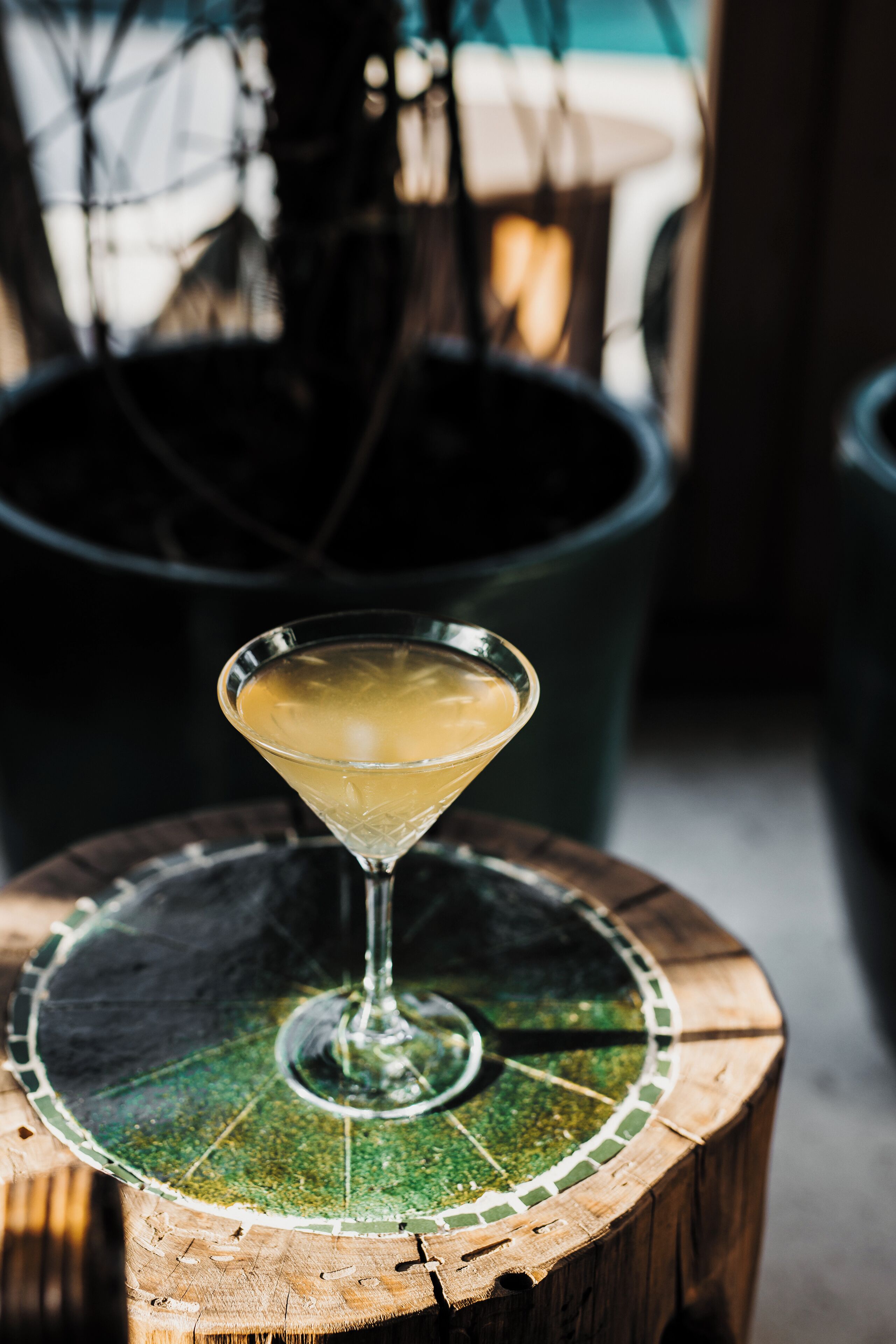 Un verre à martini posé sur une table en bois, avec un dessous de verre en mosaïque.