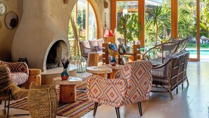 A spacious living area with a high wooden ceiling, a fireplace, comfortable seating, and large windows offering a view of the outdoors. - Pachamama Alacati  (Cesme)