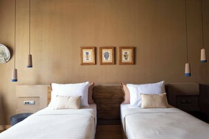 Quarto de hotel com duas camas, uma cabeceira de madeira e três quadros na parede.