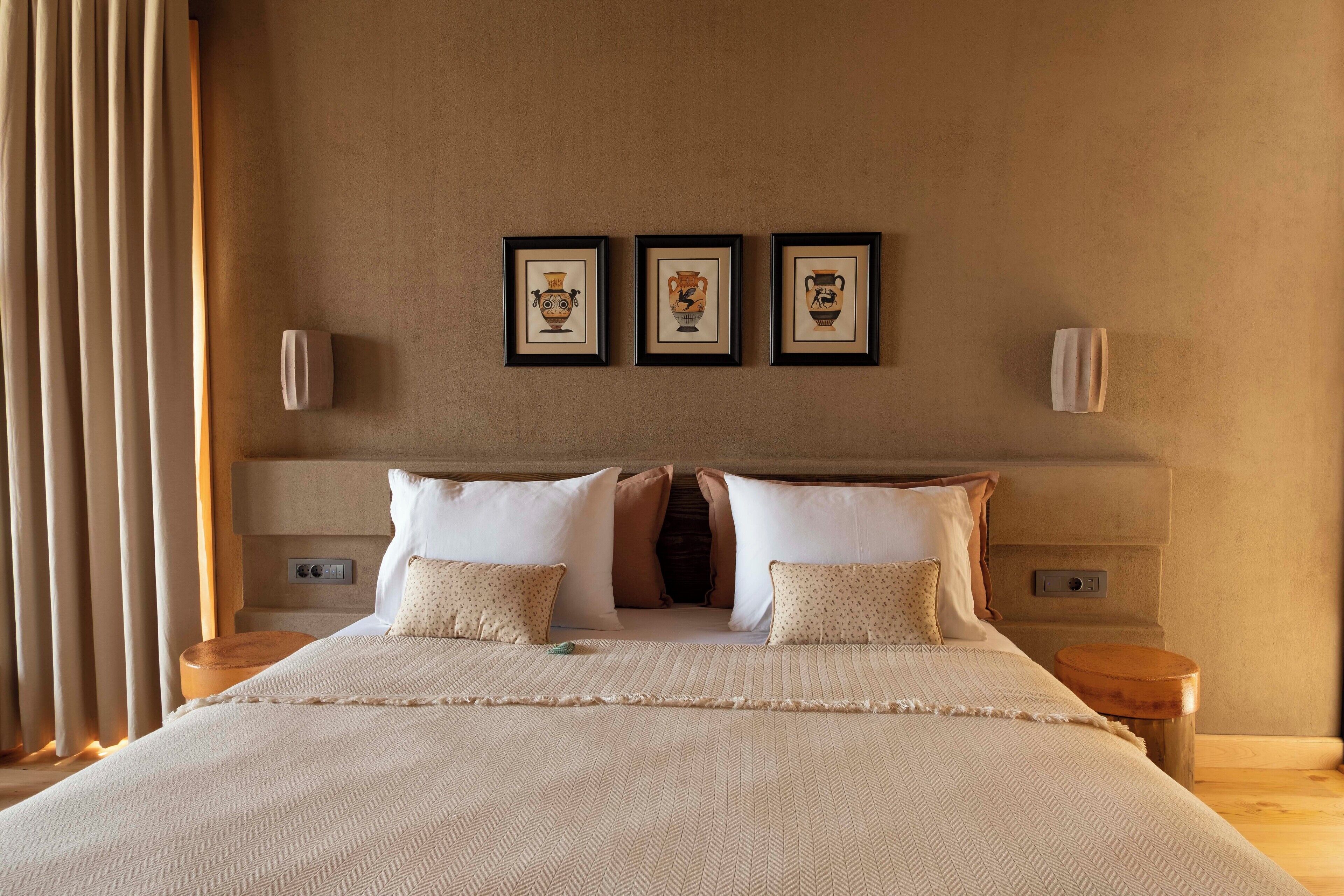 A bedroom with a large bed, a headboard, a nightstand, and three framed pictures on the wall.
