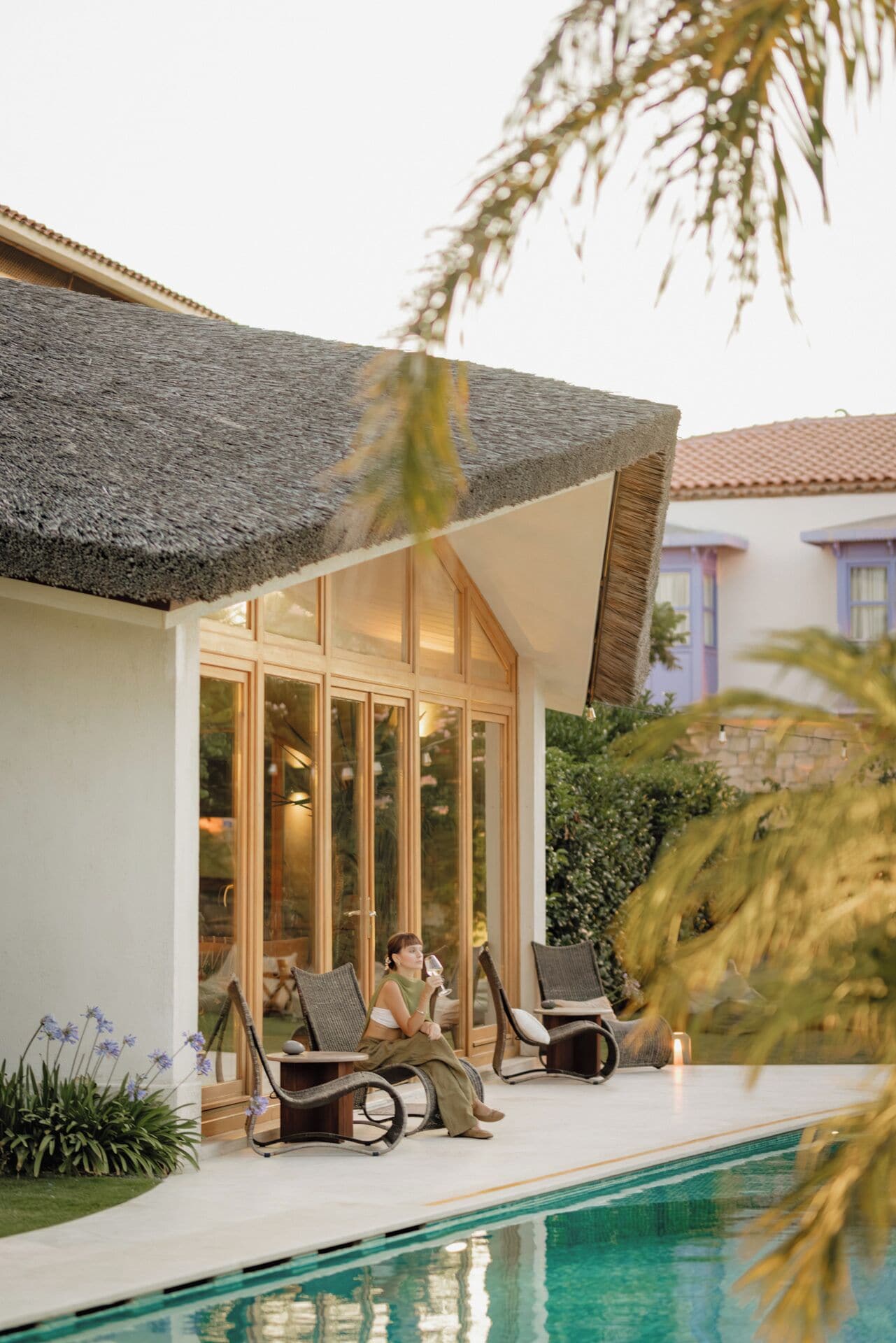 Et moderne hus med pool, med en glasindhegnet patio med siddepladser og stråtækt tag.