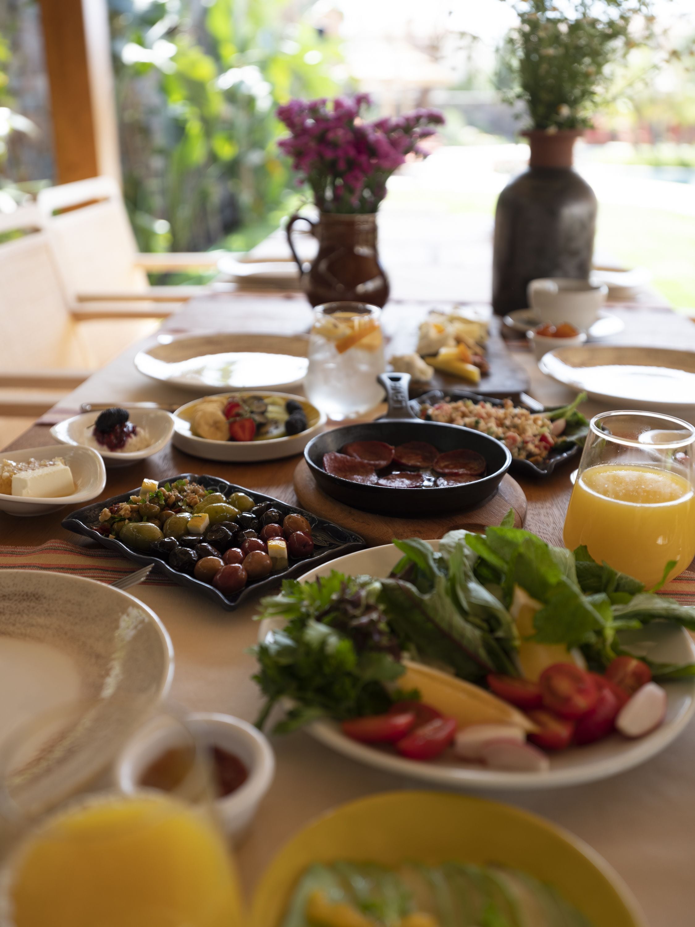 Una mesa de desayuno con diversos platos, frutas, verduras y un vaso de zumo de naranja.
