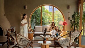 A cozy indoor space with a round window, wicker chairs, a sofa, and a small table with a vase. - Pachamama Alacati  (Cesme)