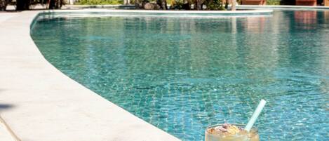 A pool with a drink on the edge, surrounded by palm trees and a clear sky.